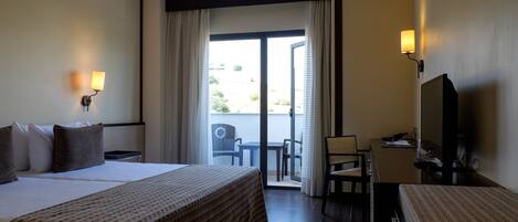 A hotel room with a large bed, a desk with a chair, a television, and a balcony with curtains.