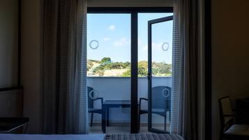 Habitación de hotel con cama, una mesita, dos sillas y un balcón con vistas al paisaje.