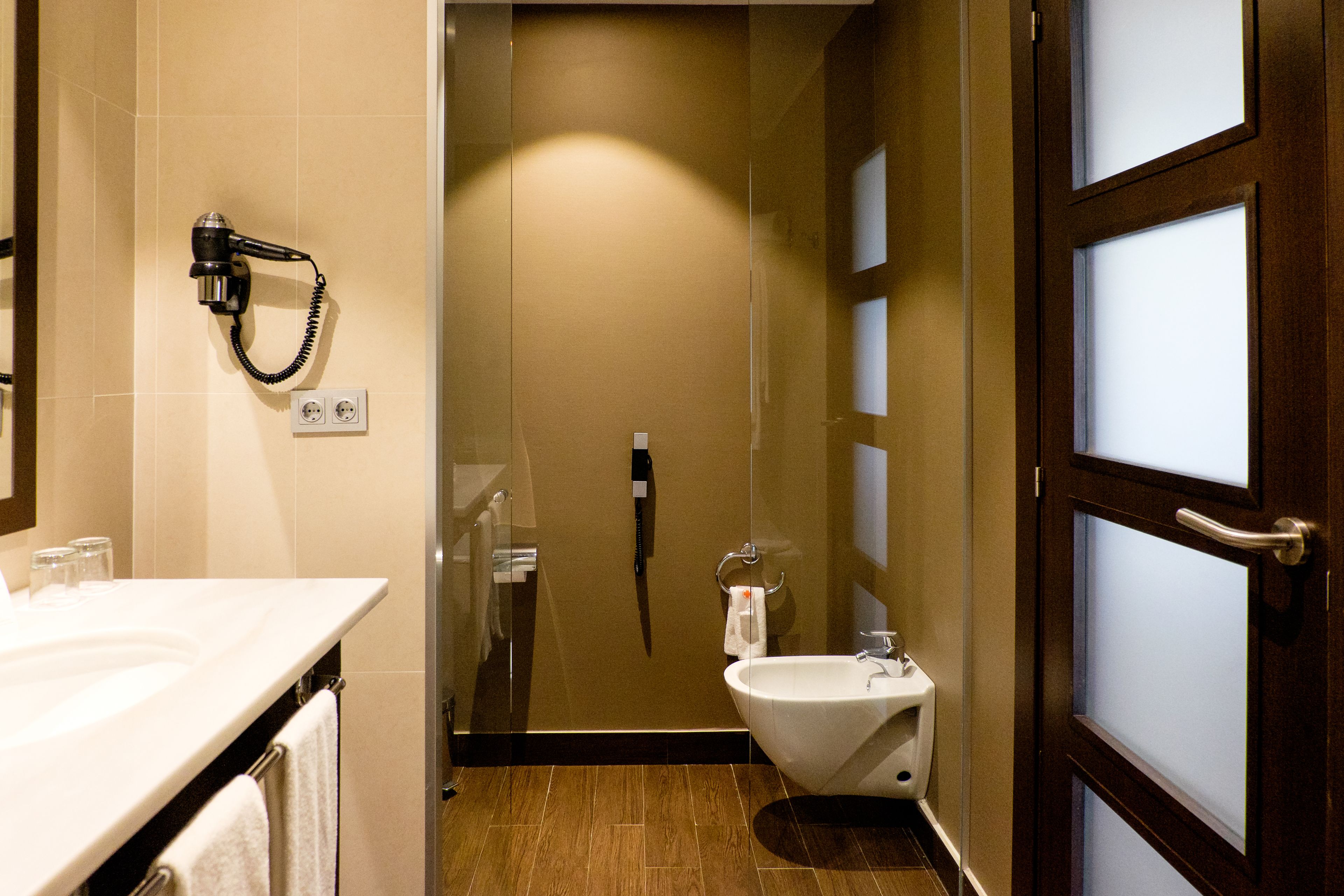 A bathroom with a shower, toilet, and hairdryer on the wall.