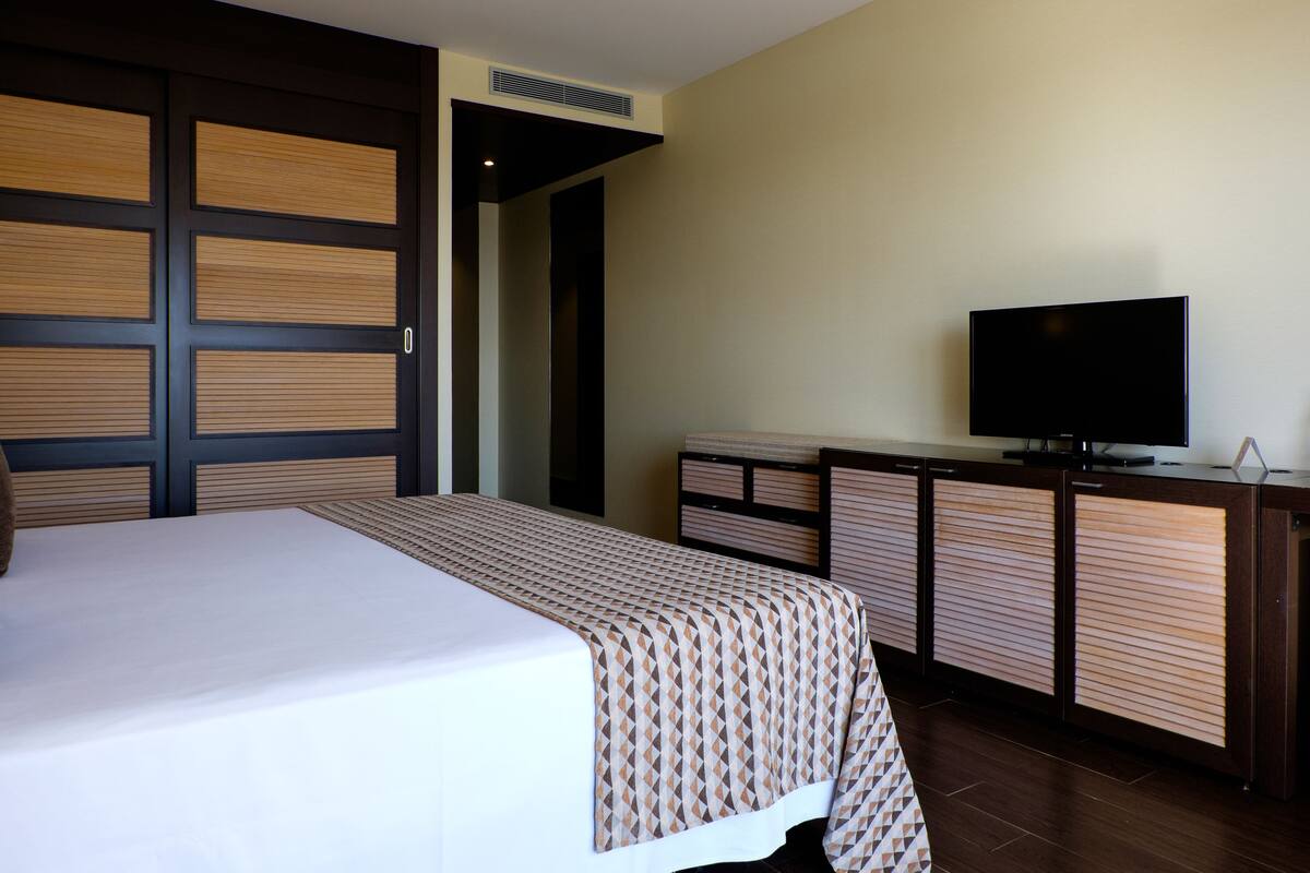 Une chambre d’hôtel avec un grand lit, une télévision et une armoire en bois.