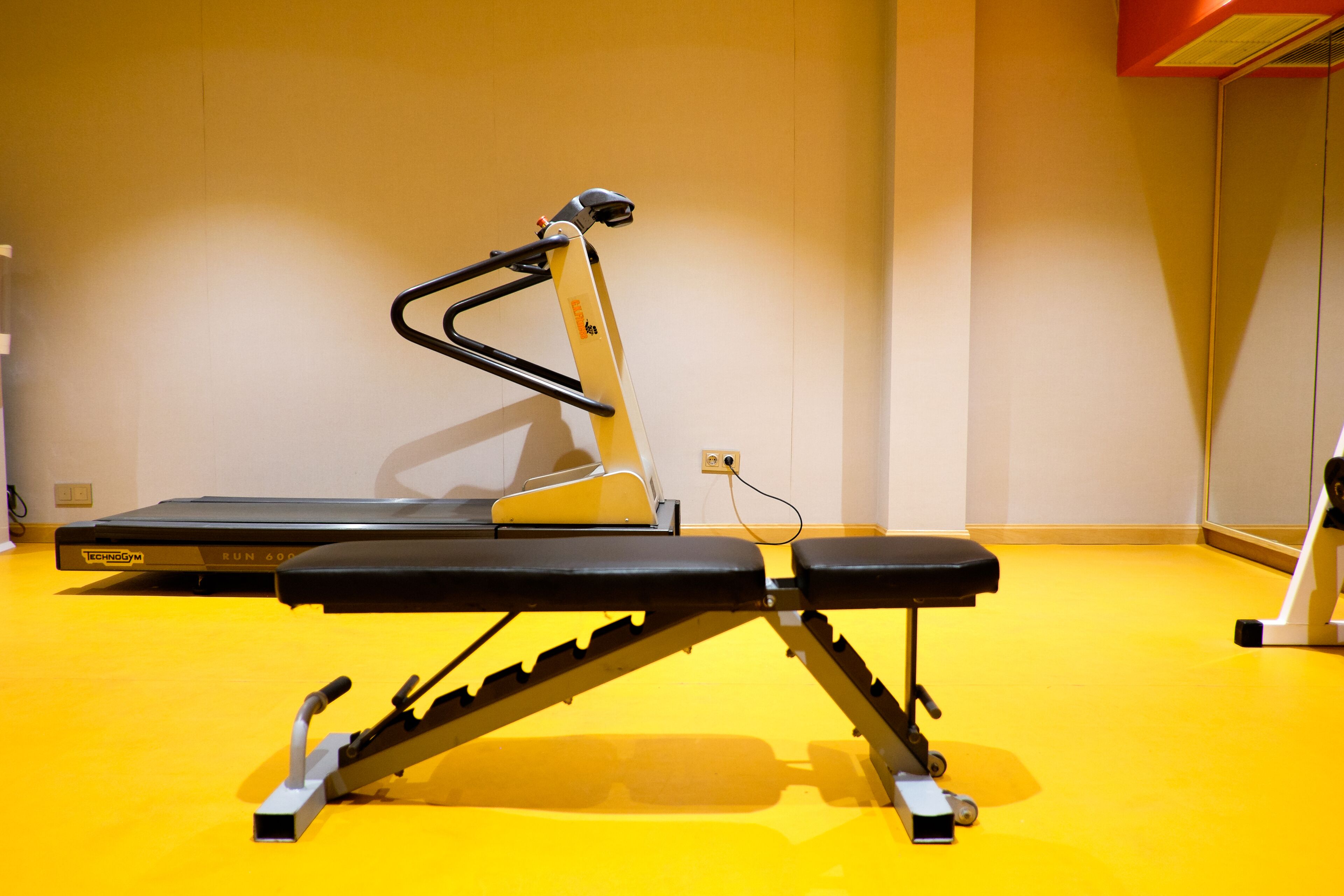 A gym with a treadmill, a bench, and a weight machine.