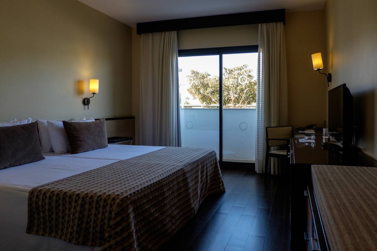 Une chambre d’hôtel avec un grand lit, deux lampes de chevet, un bureau et une vue sur l’extérieur grâce à une porte coulissante.