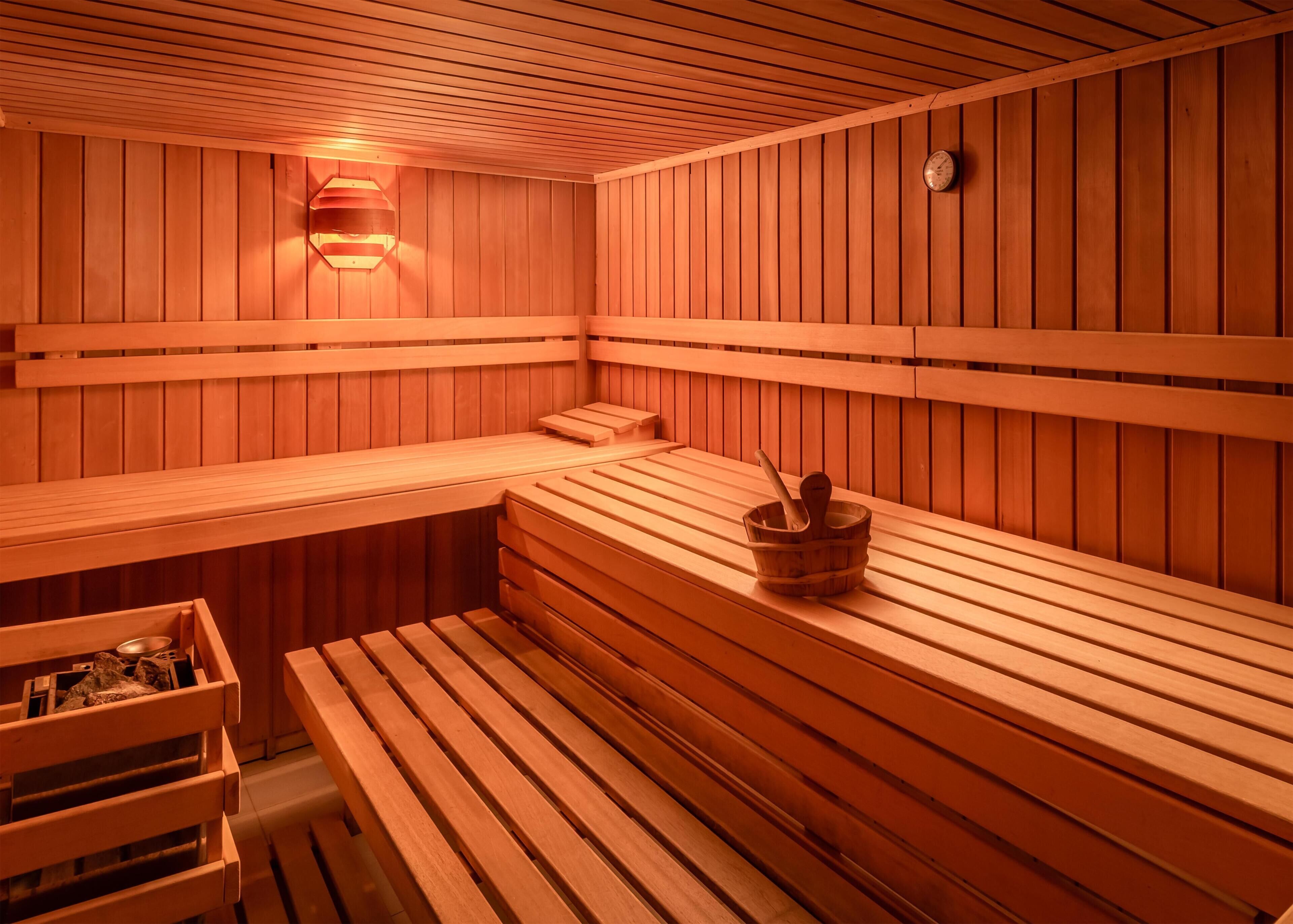 Una sauna con bancos de madera y un cubo de madera con un cepillo.