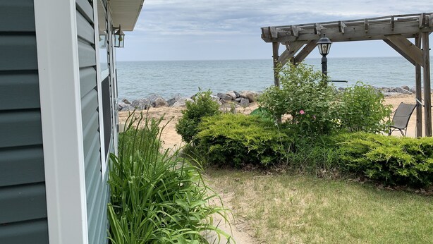 Un patio con vista al océano, una pérgola de madera y una playa con rocas.