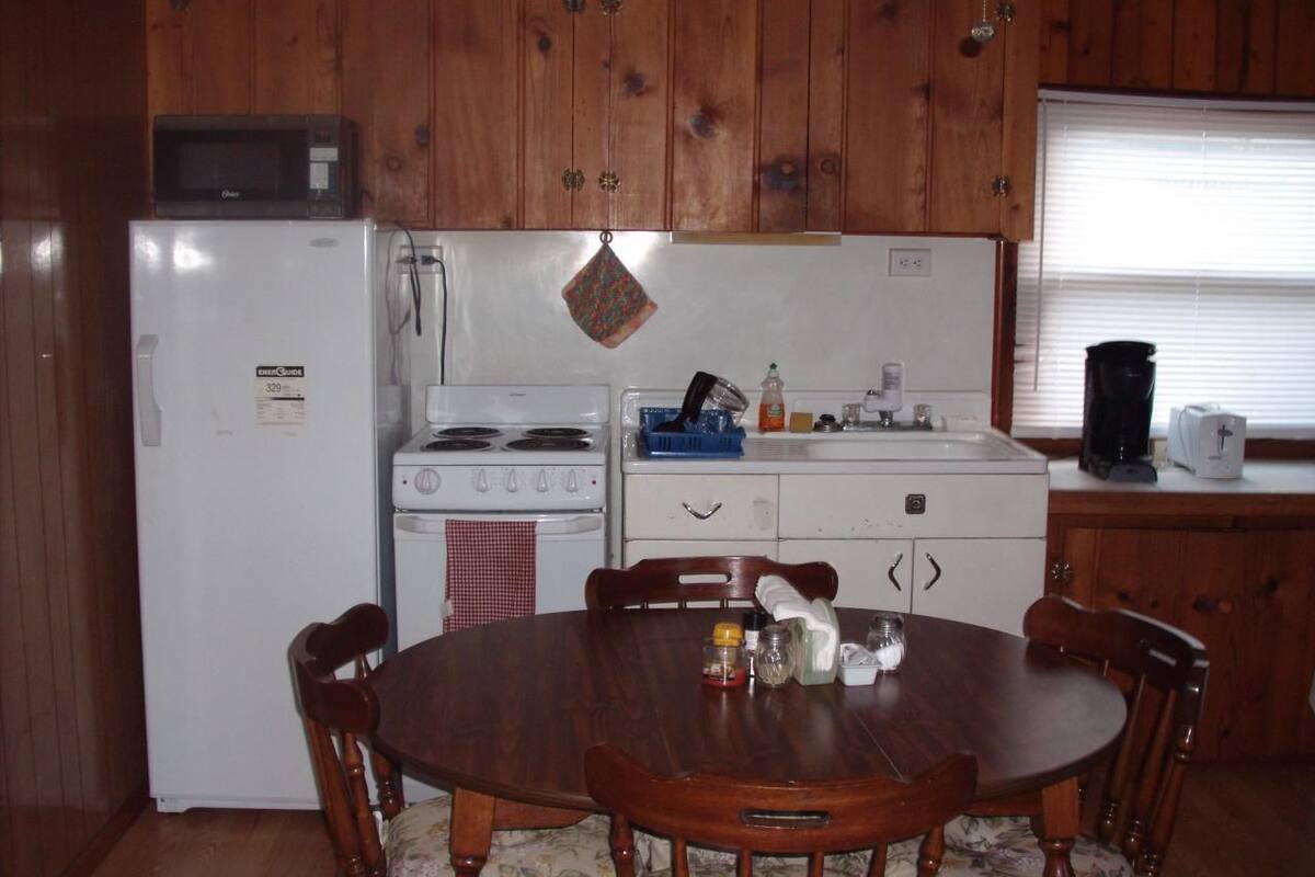 A compact kitchen with wooden cabinets, a white refrigerator, a stove, and a dining table with chairs.