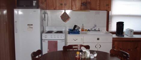 A compact kitchen with wooden cabinets, a white refrigerator, a stove, and a dining table with chairs.
