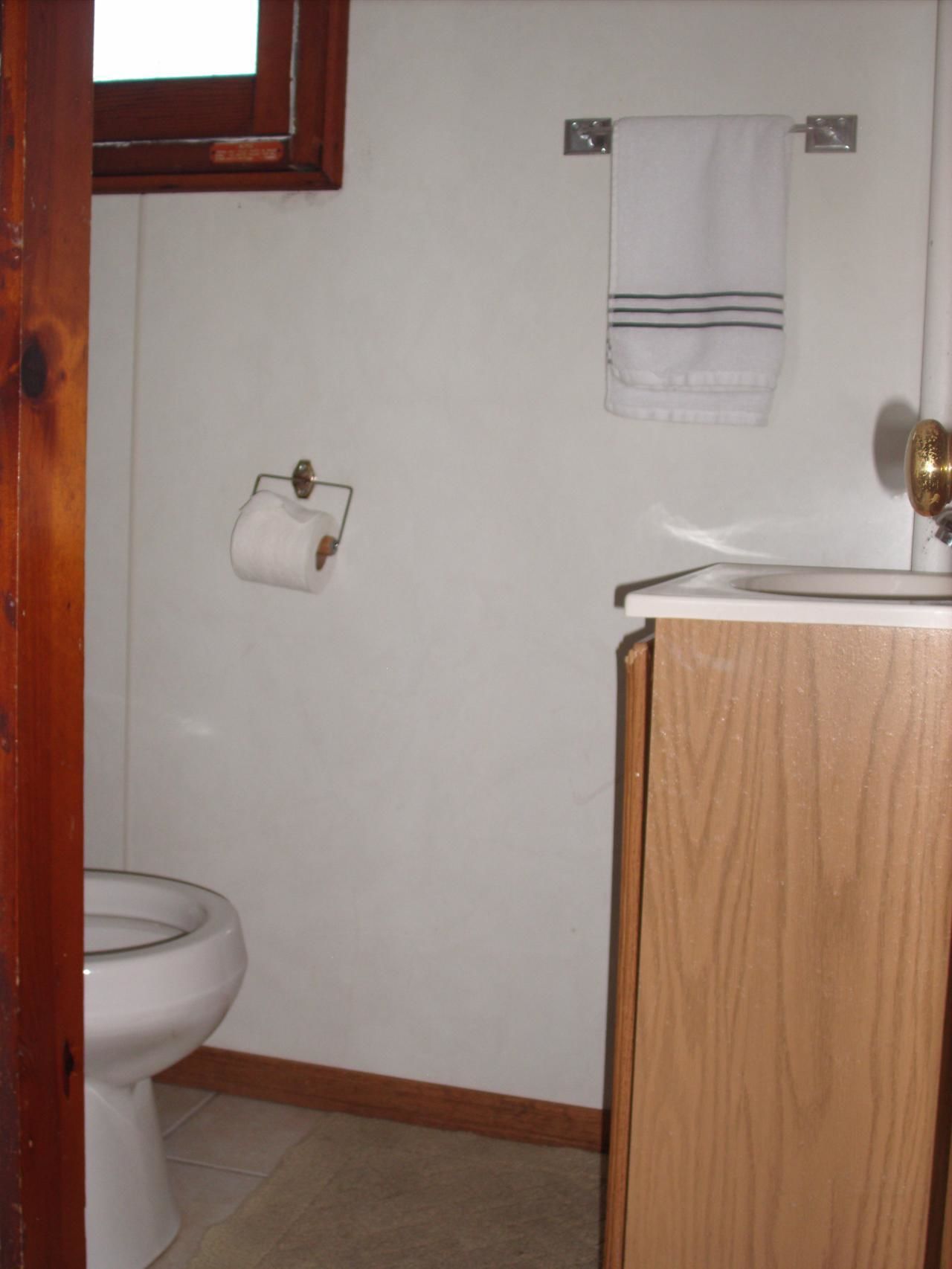 A small bathroom with a toilet, a wooden cabinet, and a towel hanging on a metal hook.