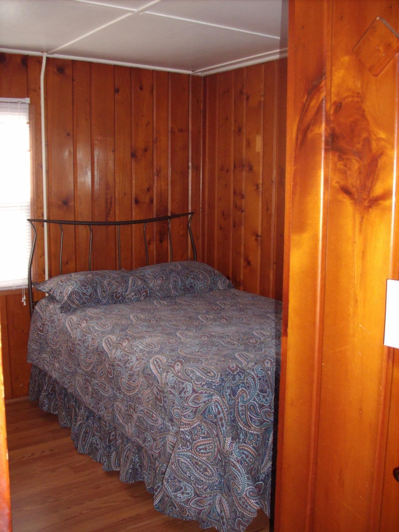 A bedroom with wooden walls, a bed with a patterned bedspread, and a metal headboard.