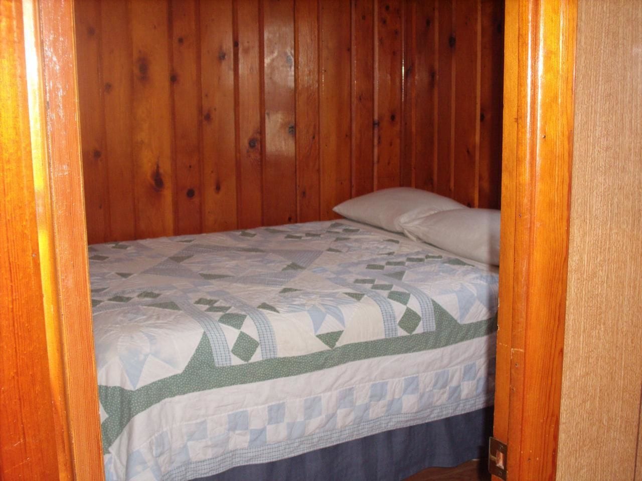 A wooden-paneled room with a bed featuring a quilted bedspread.