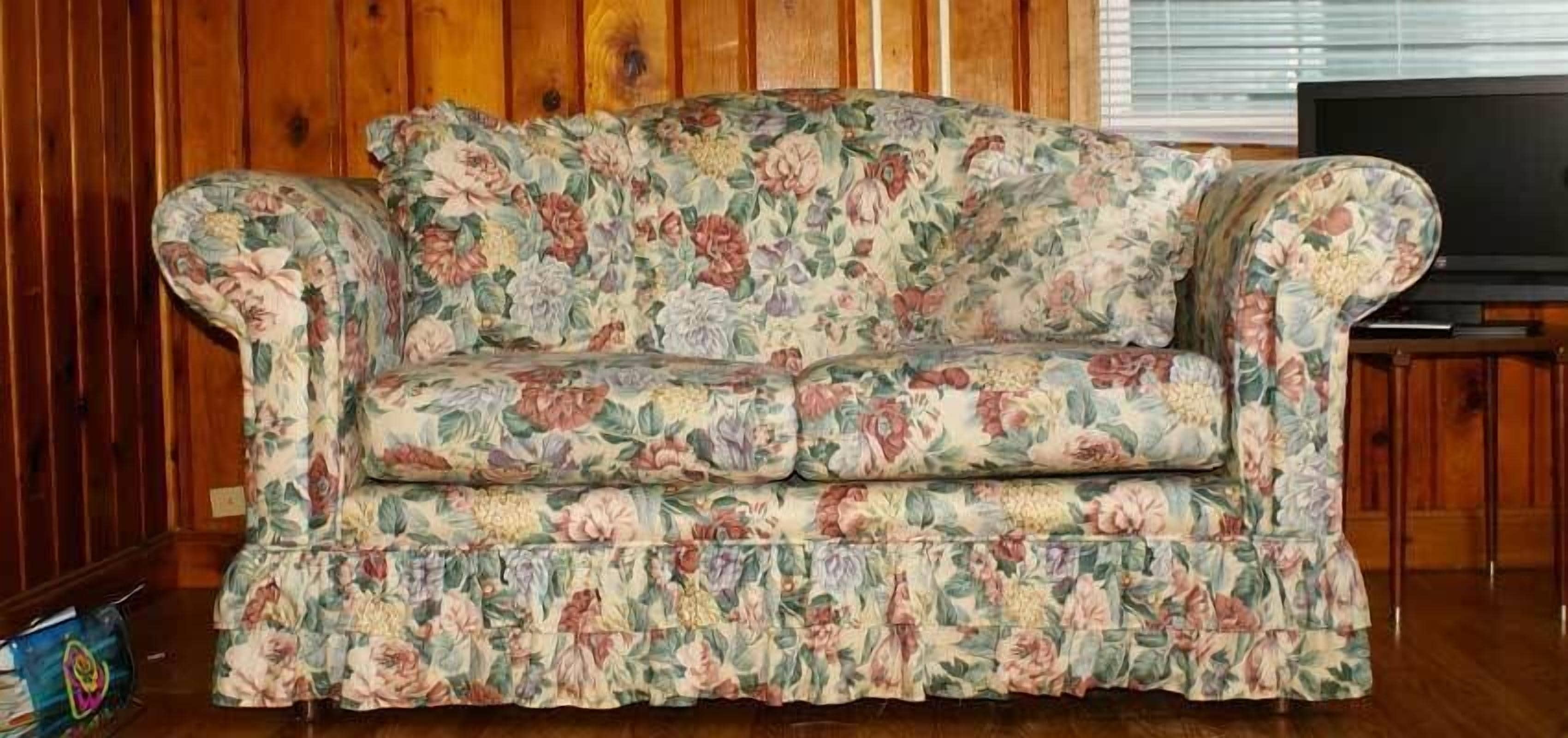 Un canapé à motifs floraux dans une pièce aux murs lambrissés et équipée d’un téléviseur.