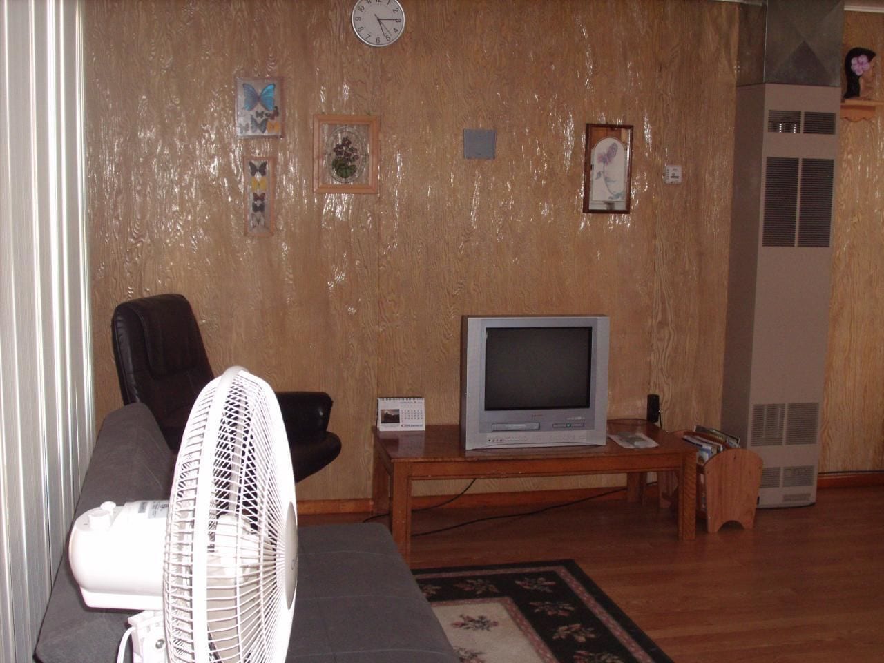 Un salon avec une télévision, un ventilateur et une horloge au mur.