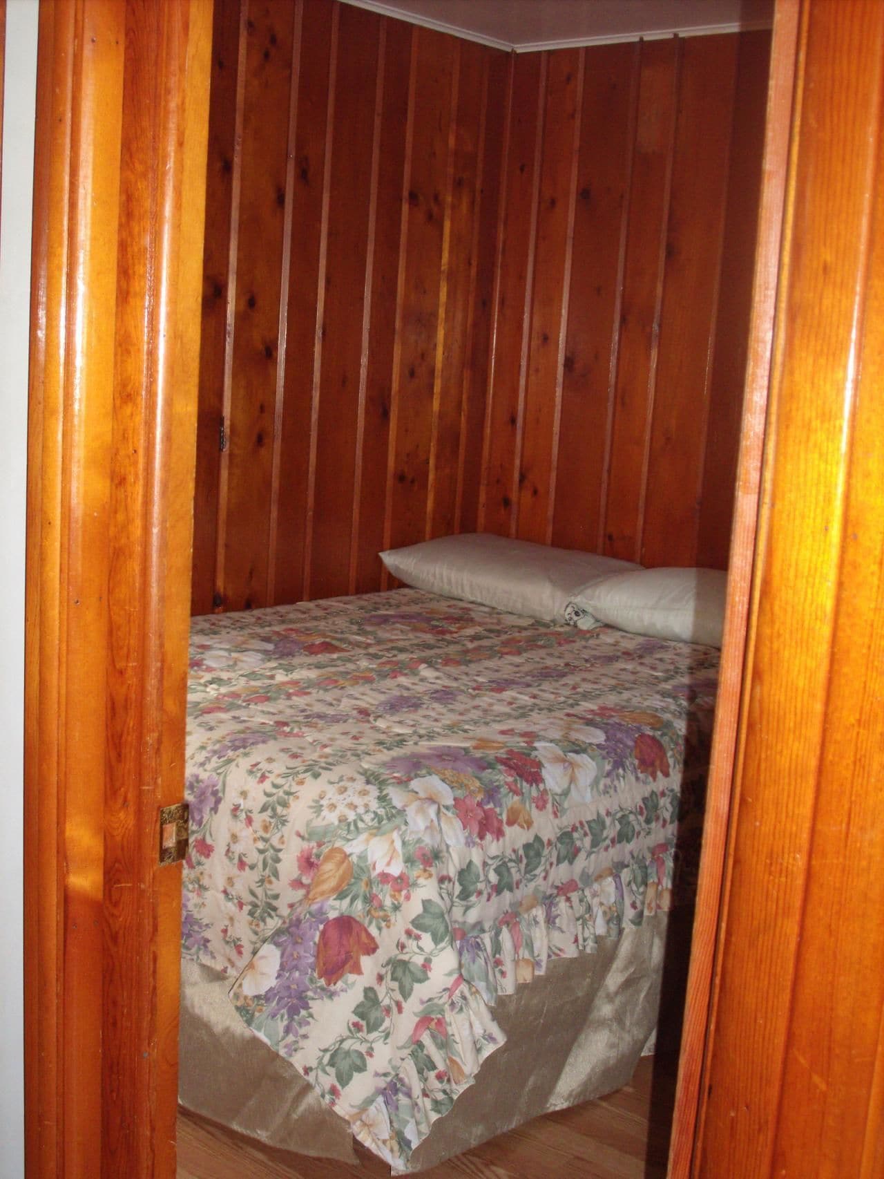 A bedroom with wooden walls, a floral bedspread, and a white pillow.