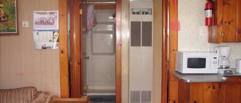 A compact living space with a kitchenette, a wooden door leading to a bathroom, and a small seating area.