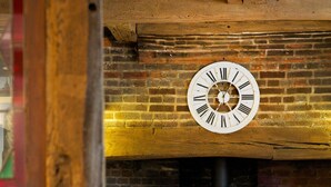 A rustic interior with a brick fireplace, a wooden ceiling, and a clock on the wall. - The Queen's Inn (Cranbrook)