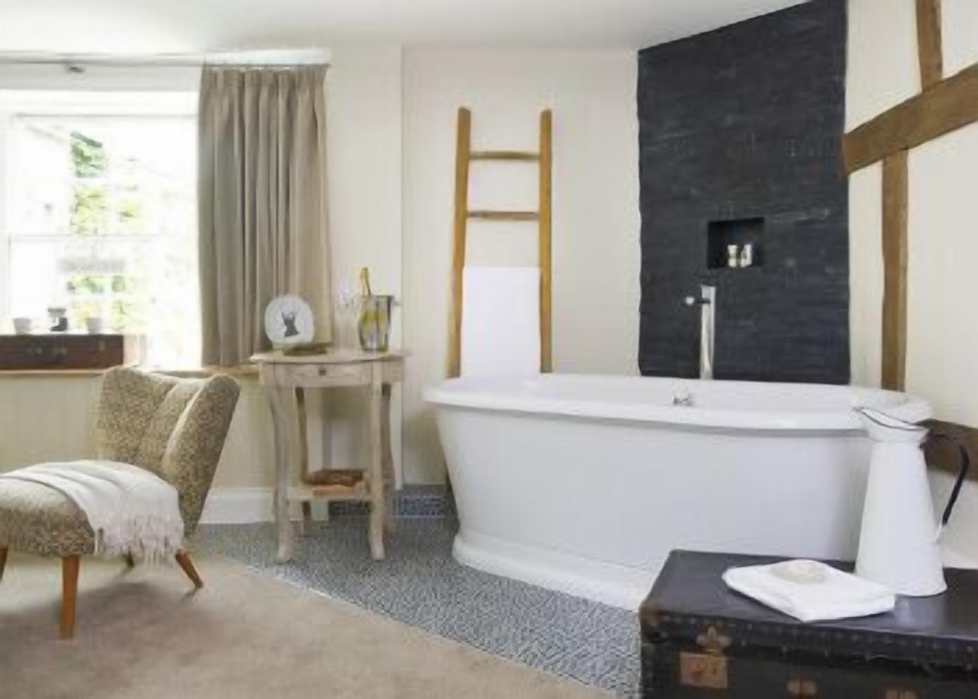 A bathroom with a freestanding bathtub, a wooden ladder, and a dark accent wall.