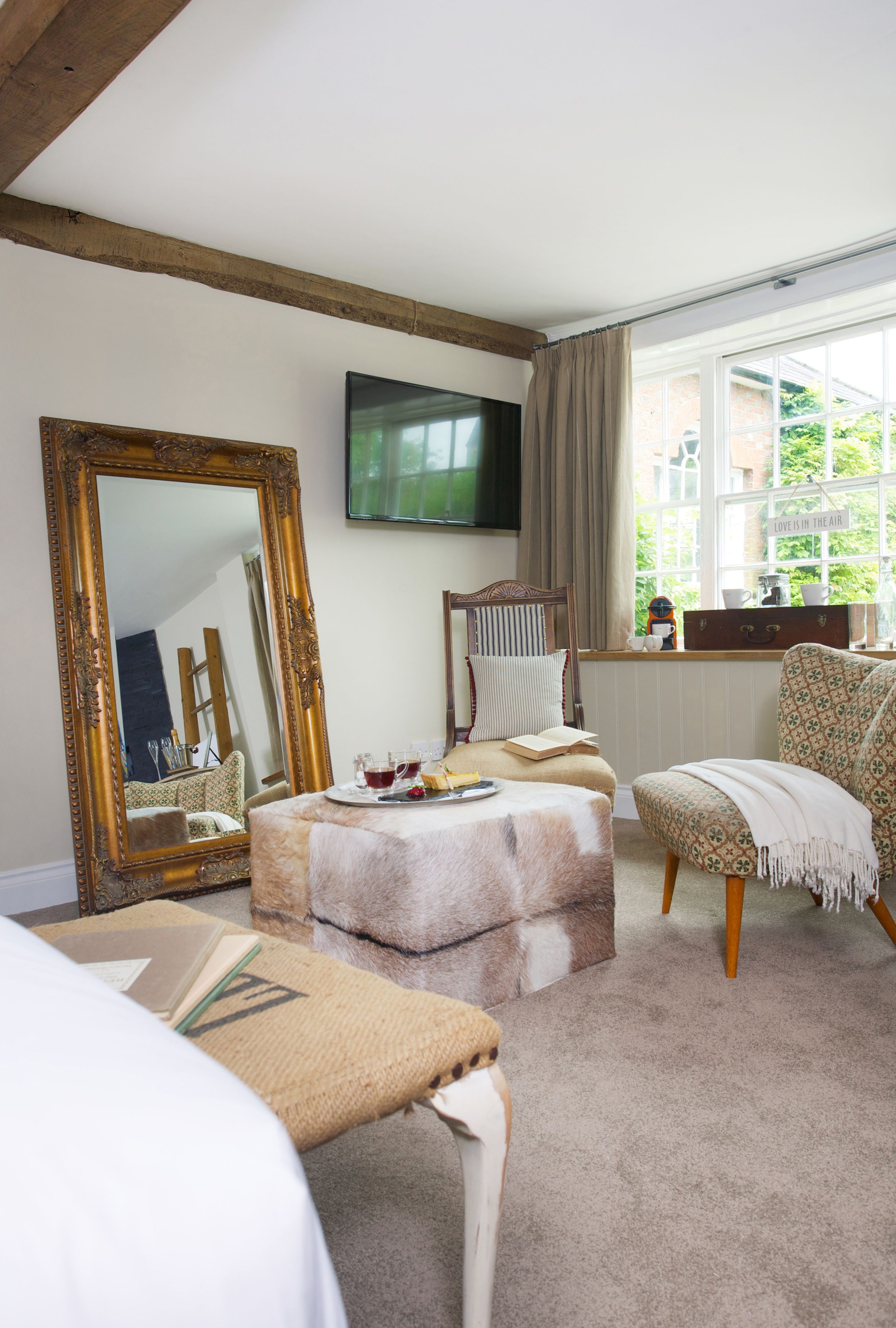 A cozy room with a large mirror, a television, a comfortable chair, and a window with a view of greenery.
