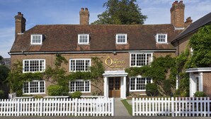 A traditional brick building with a sign reading "The Queen's Inn." It features multiple windows, a white picket fence, and a brick chimney. - The Queen's Inn (Cranbrook)