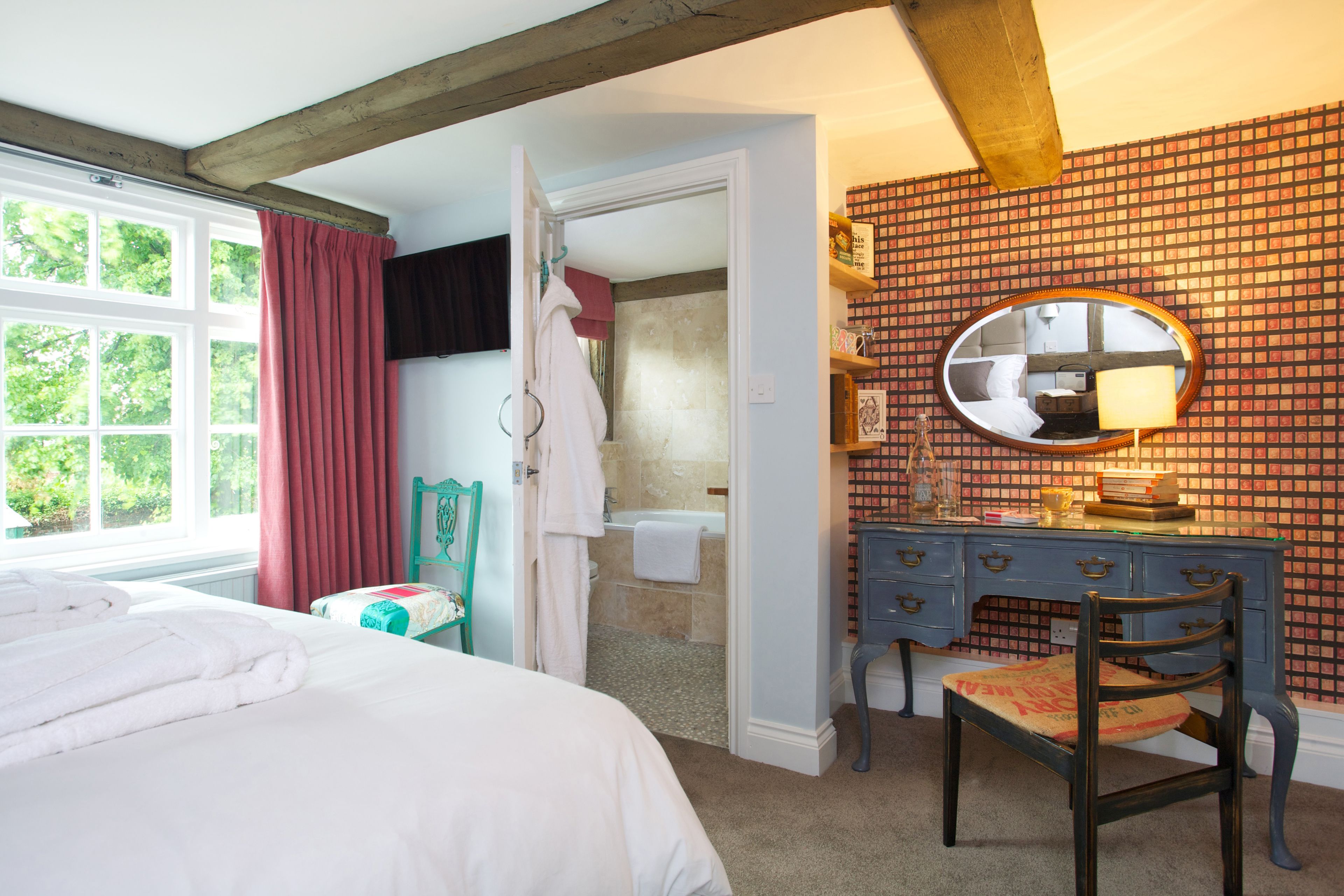 A bedroom with a large bed, a desk with a chair, a mirror, and a bathroom visible through an open door.