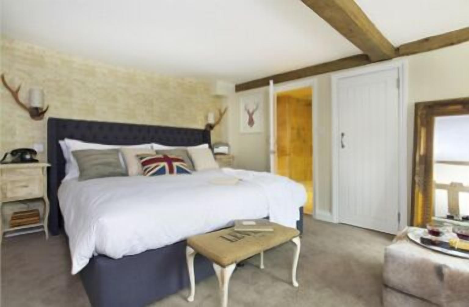 Een slaapkamer met een groot bed, een nachtkastje, een bankje en een garderobe.