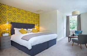 Een slaapkamer met een groot bed, een nachtkastje, een stoel en een raam met gordijnen.
