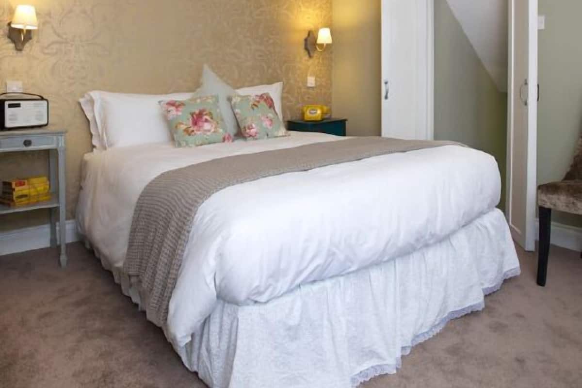 Un dormitorio con una cama grande, dos mesitas de noche, una silla y una puerta.