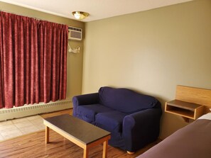 A room with a sofa, a small table, a wooden nightstand, a red curtain, and a ceiling light fixture. - Stars Inn & Suites Building B (Fort Saskatchewan)