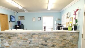 A reception area with a stone counter, a wooden door, a security camera, a television, and a window with blinds. - Stars Inn & Suites Building B (Fort Saskatchewan)