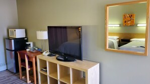 A hotel room with a TV on a wooden stand, a microwave, a coffee maker, a lamp, and a bed with a headboard. - Stars Inn & Suites Building B (Fort Saskatchewan)