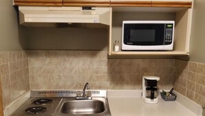 A compact kitchen with a stove, sink, microwave, and a coffee maker. - Stars Inn & Suites Building B (Fort Saskatchewan)