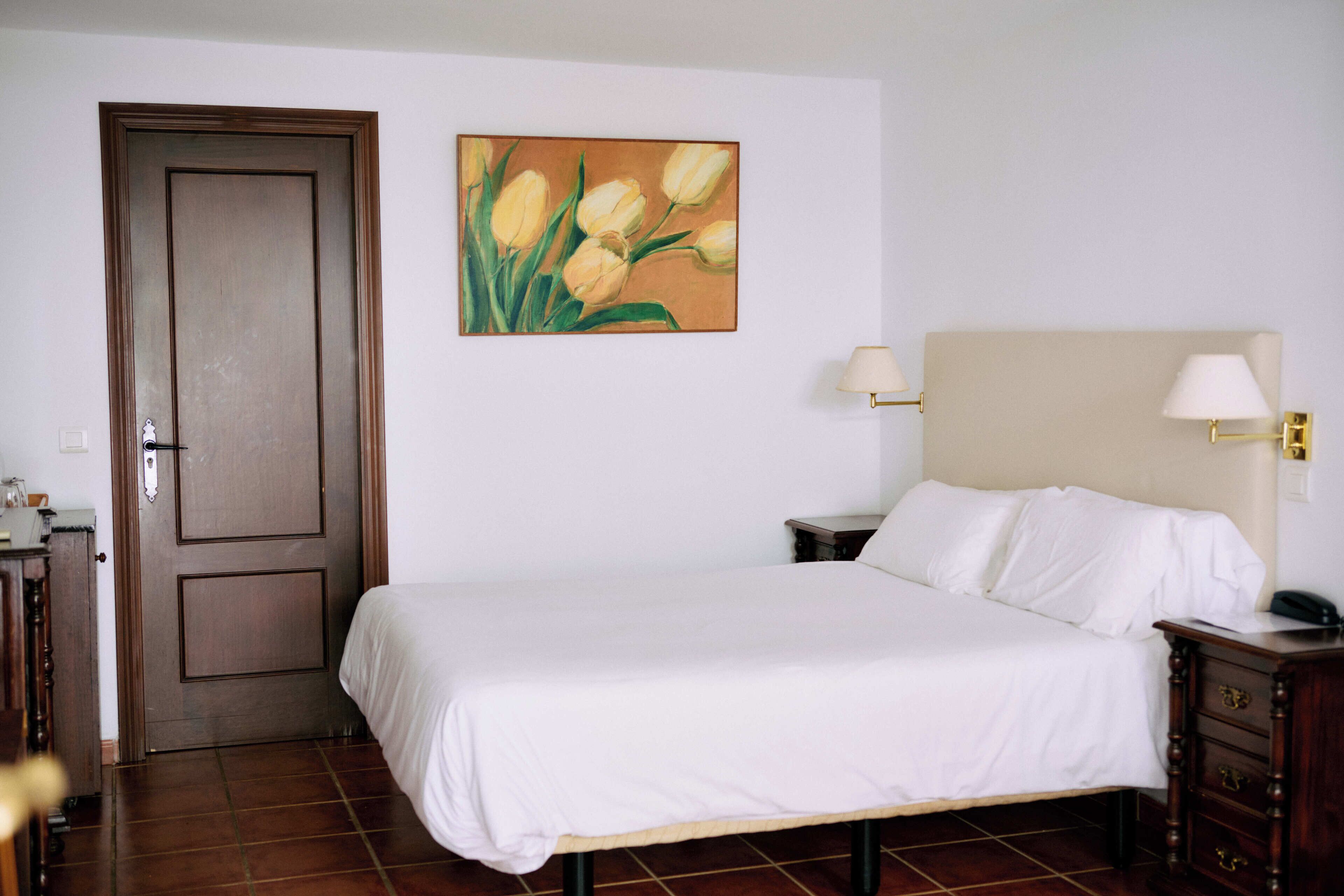 Ein Hotelzimmer mit einem Bett, Nachttischen, einem Gemälde und einer Tür.