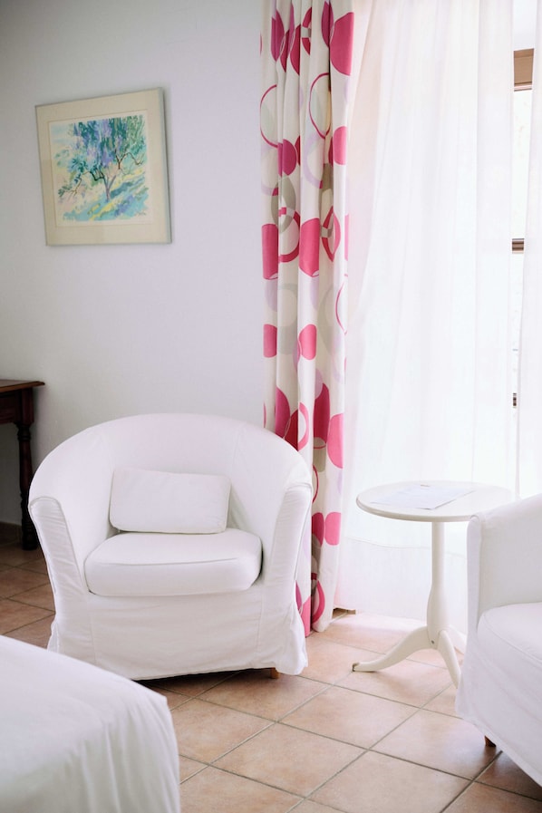 A room with a white armchair, a small round table, and a bed. - Molino del Santo (Benaojan)