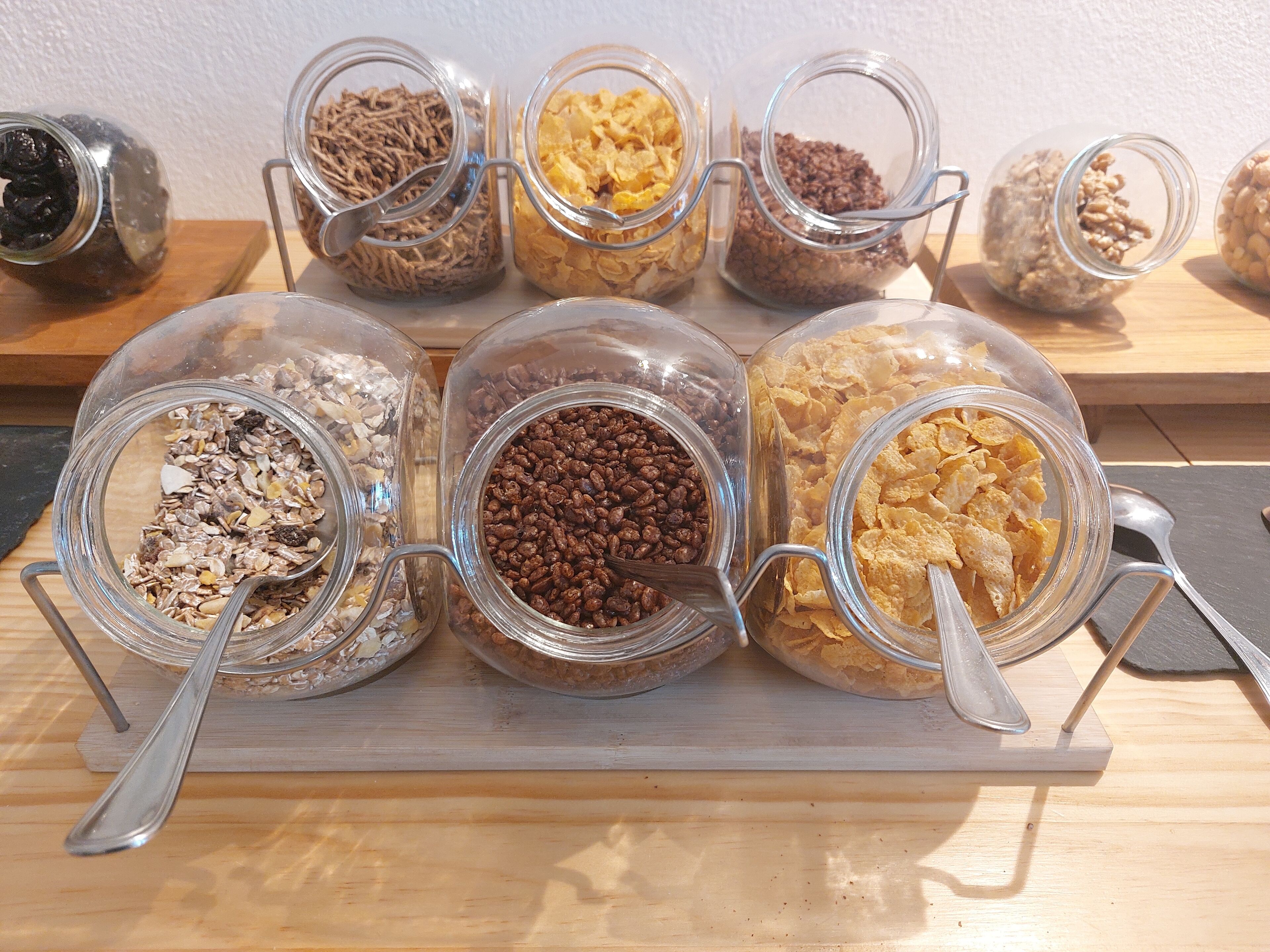 A wooden shelf with multiple glass jars containing various food items like nuts, seeds, and cereal flakes.