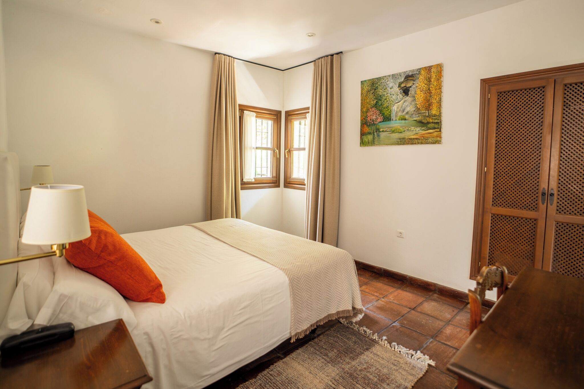 Une chambre à coucher comprenant un lit, une table de chevet, une lampe, un tableau et une porte ornée d’un motif en treillis.