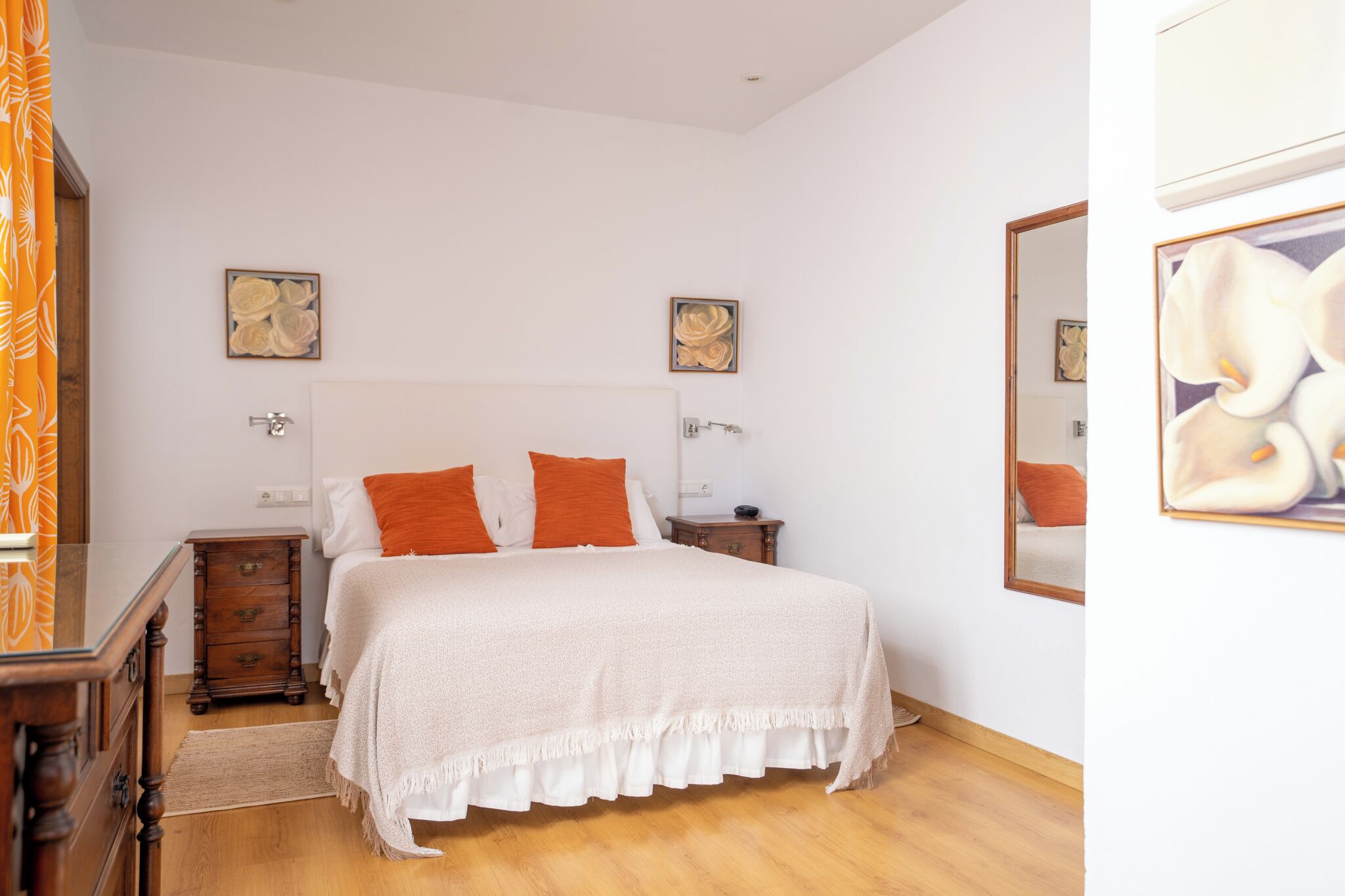 A bedroom with a bed, wooden nightstands, a dresser, and artwork on the walls.