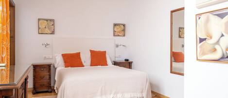 A bedroom with a bed, wooden nightstands, a dresser, and artwork on the walls.