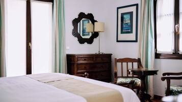 Une chambre d’hôtel avec un lit, une commode, une chaise, une table, une lampe et un tableau encadré au mur.
