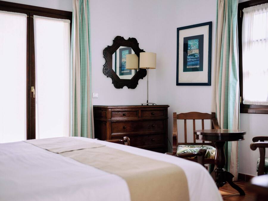 Une chambre d’hôtel avec un lit, une commode, une chaise, une table, une lampe et un tableau encadré au mur.
