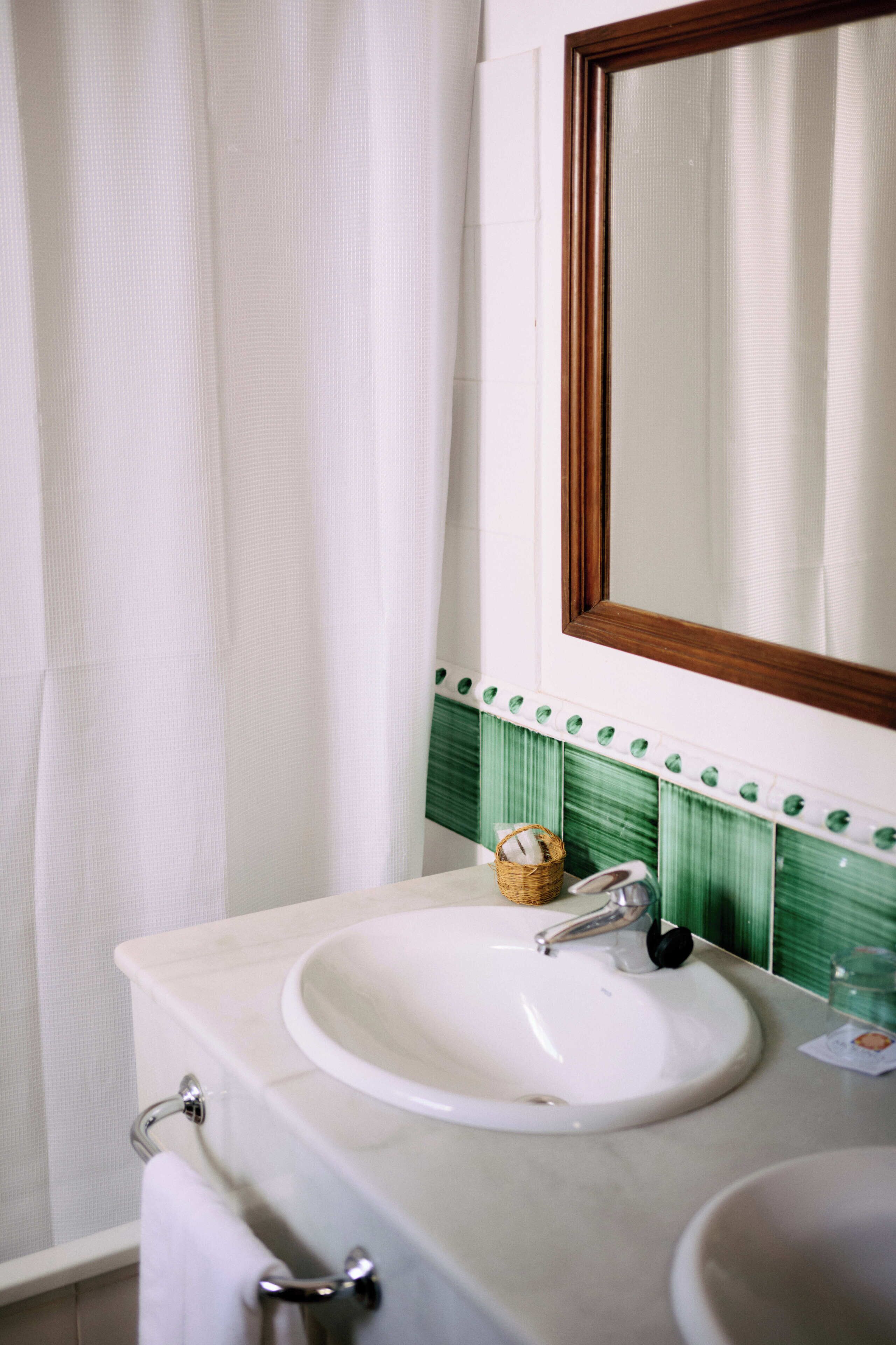 A bathroom with a white sink, a mirror, and a green tiled backsplash.