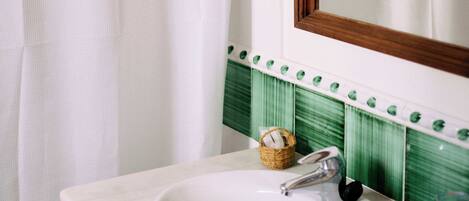 A bathroom with a white sink, a mirror, and a green tiled backsplash.