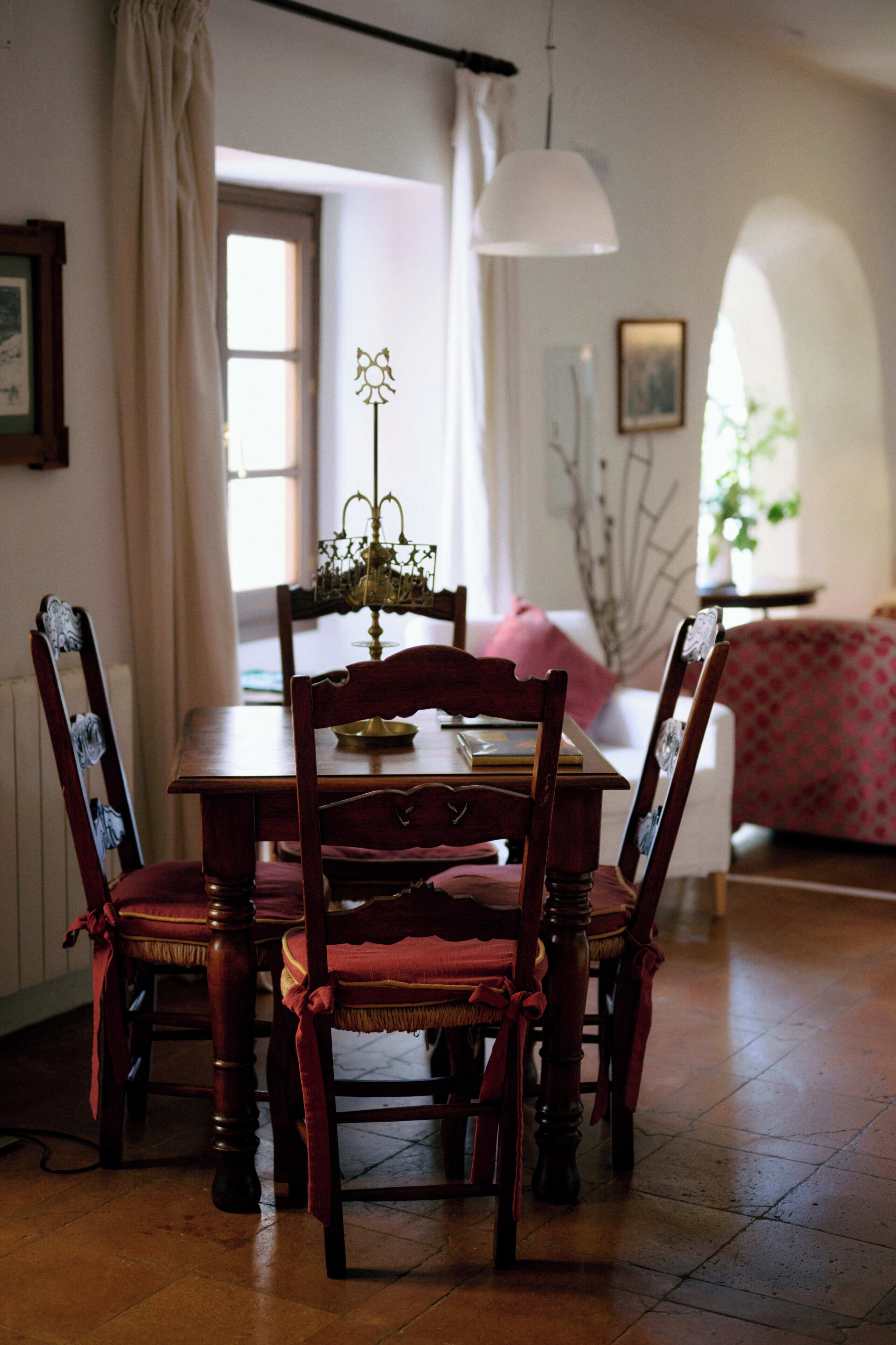 A dining area with a wooden table and chairs, a chandelier, and a view of the outdoors through a window.