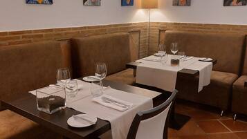 A dining area with booths and tables, each set with cutlery and glasses, and a lamp on the wall.