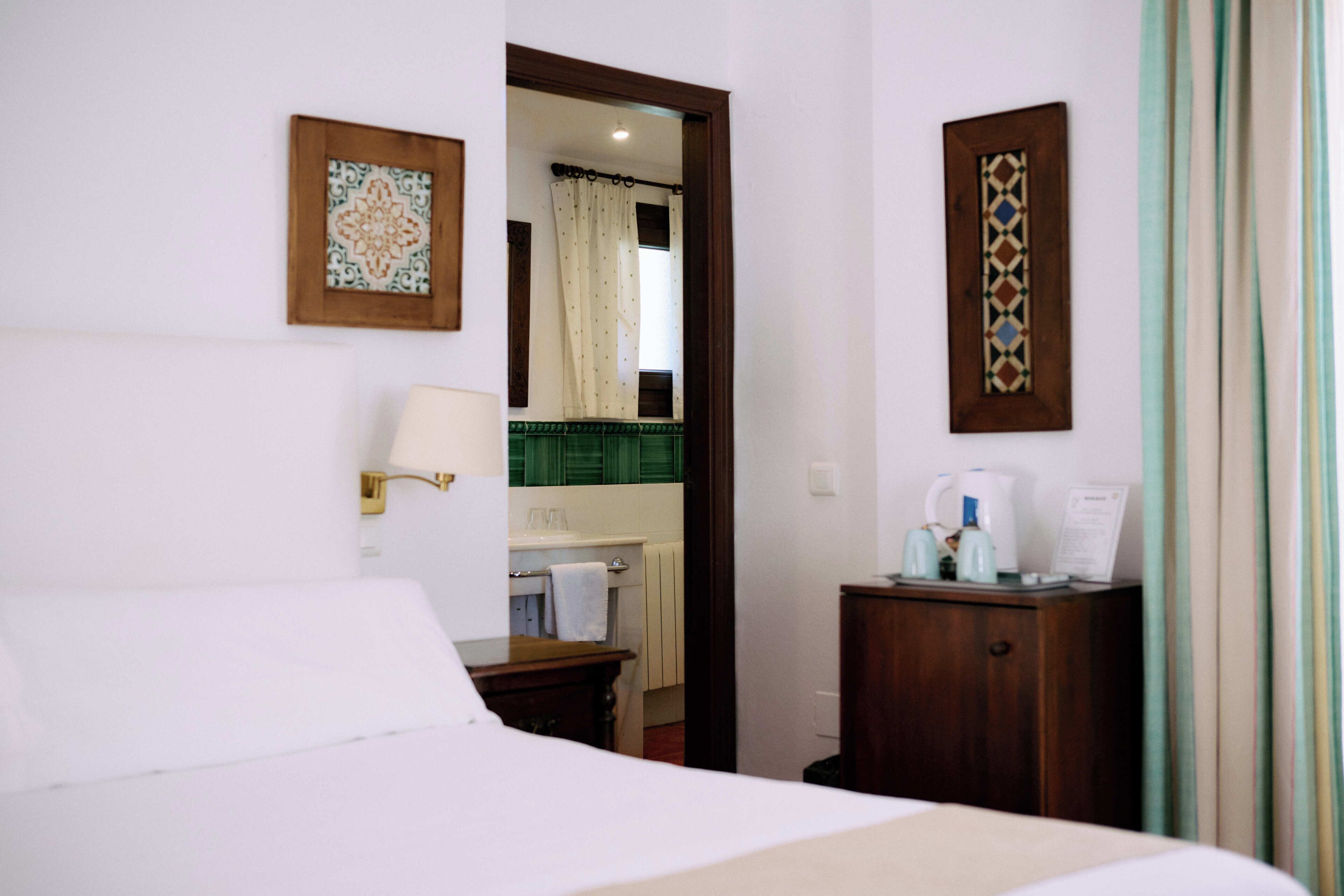 A hotel room with a bed, a bedside table with a lamp, a small cabinet, and a mirror on the wall.