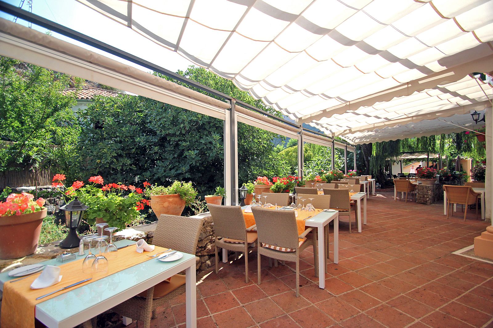 An outdoor patio with tables and chairs, surrounded by potted plants and a tiled floor.