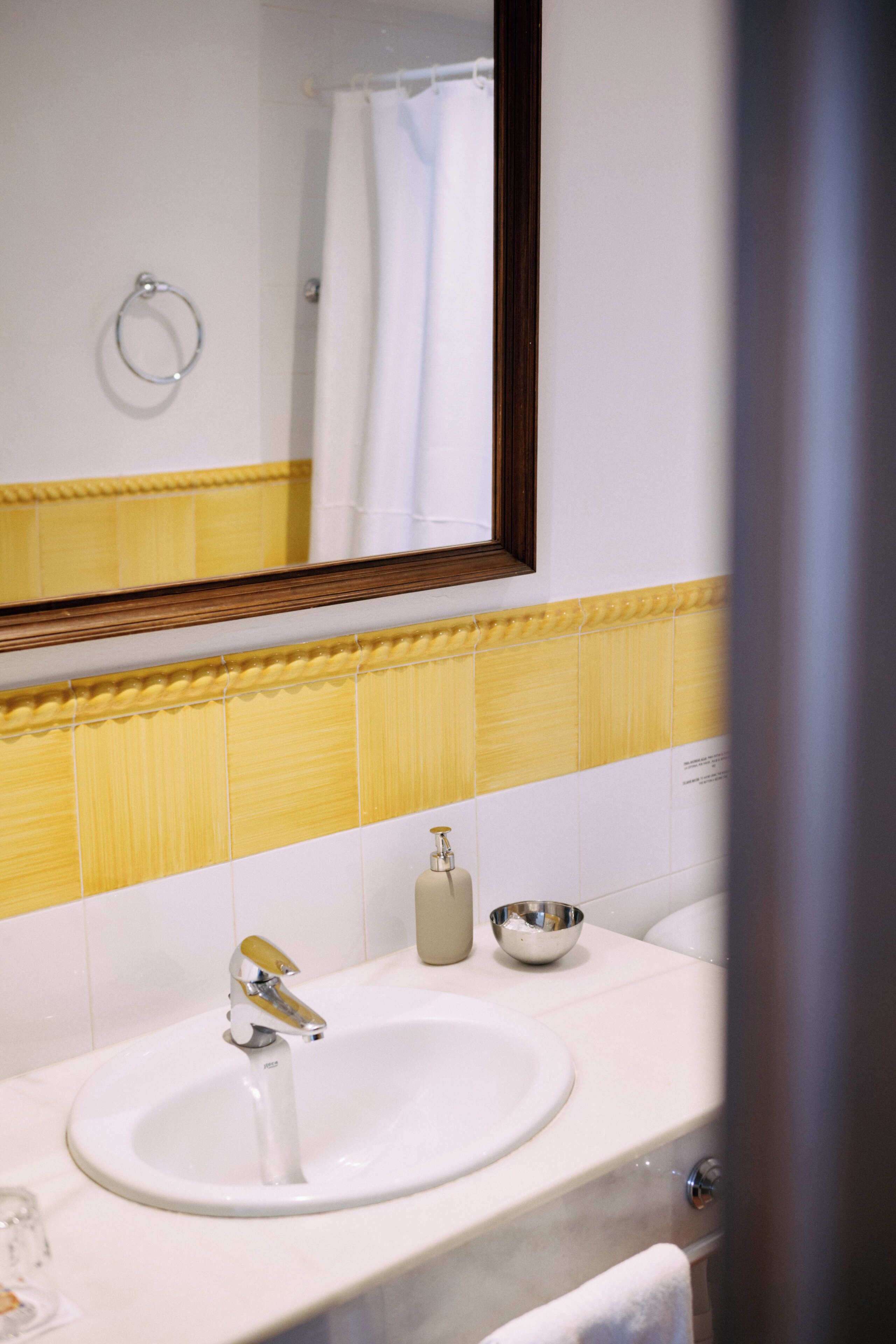 Un baño con un lavabo blanco, un espejo y una pared con azulejos amarillos.
