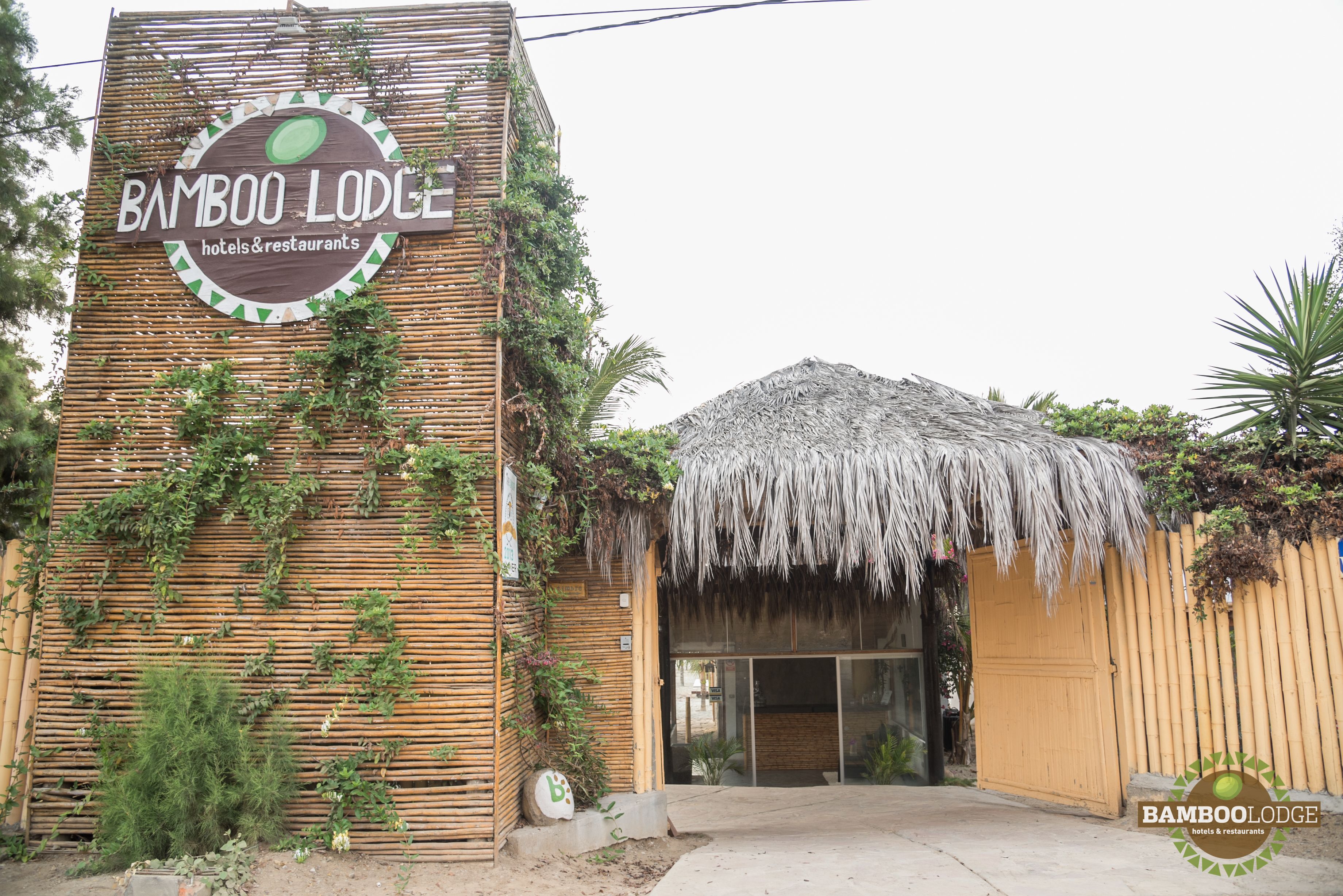 A bamboo lodge entrance with a thatched roof and a sign indicating it is a hotel and restaurant.
