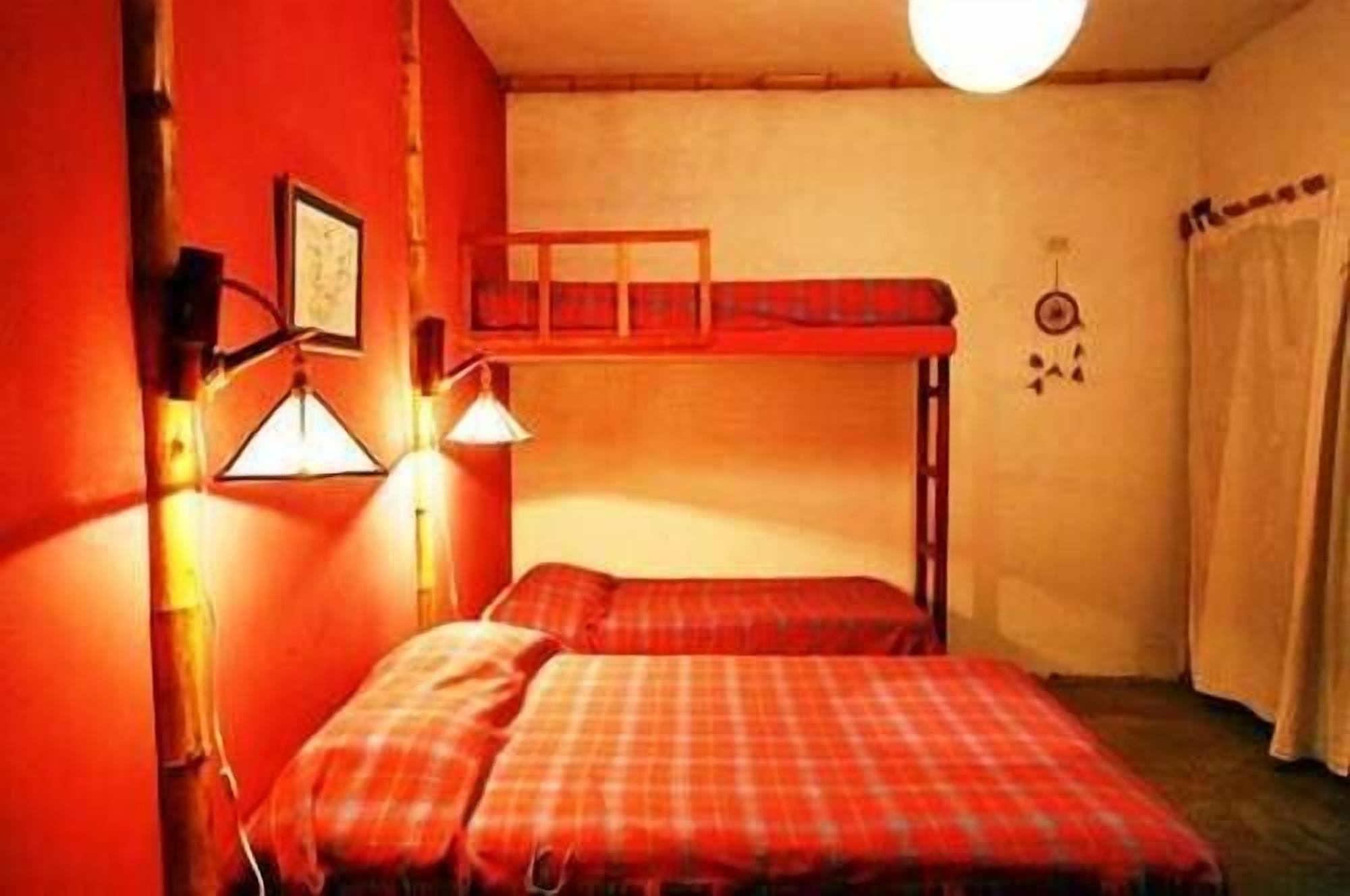 Una habitación con dos camas, una litera, una lámpara de pared y una cortina.