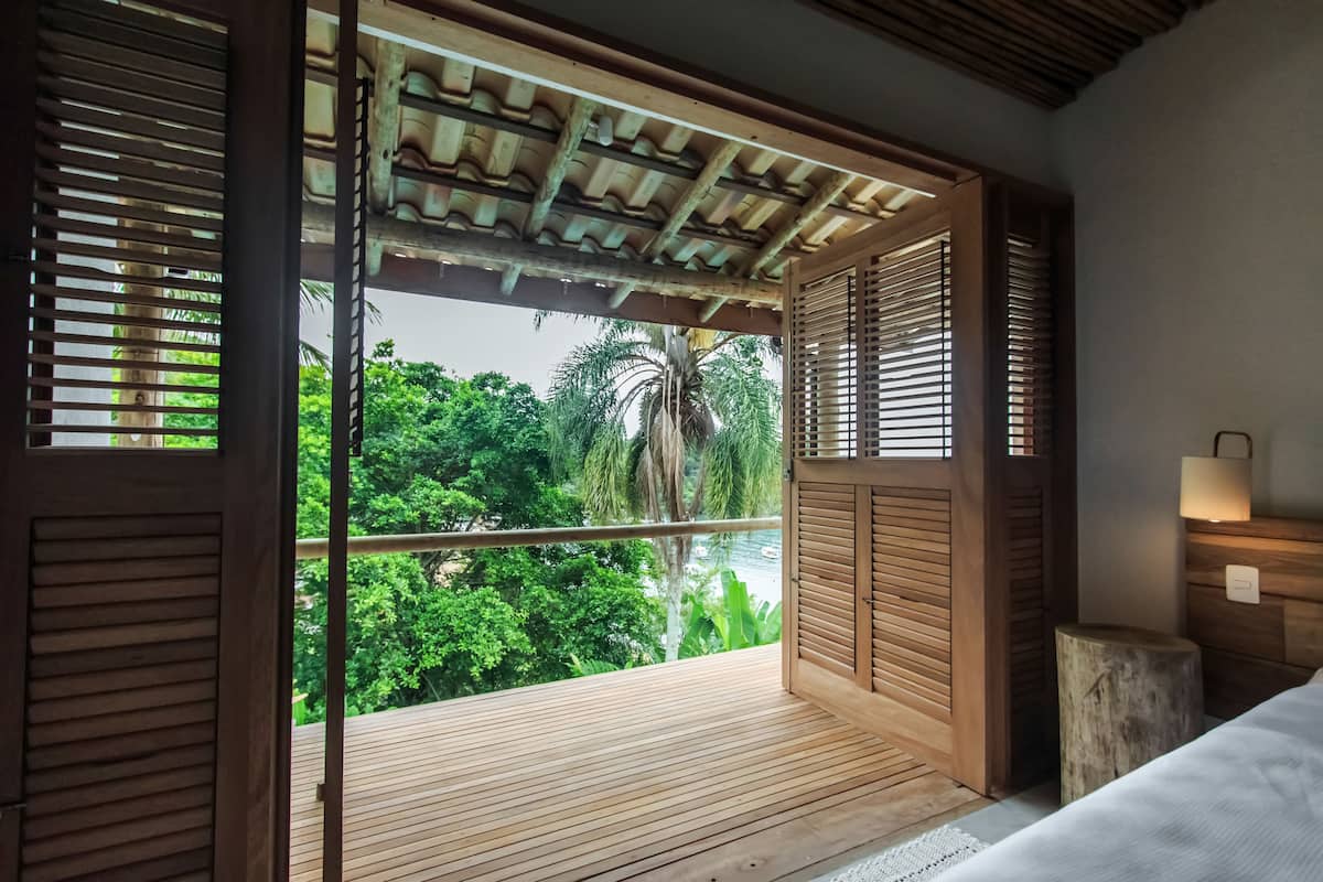 Una habitación con piso de madera, una cama, una mesita de noche y vistas a follaje exuberante y un río.