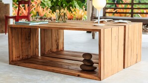 Un tavolino in legno con una pila di libri e un vaso con piante verdi.