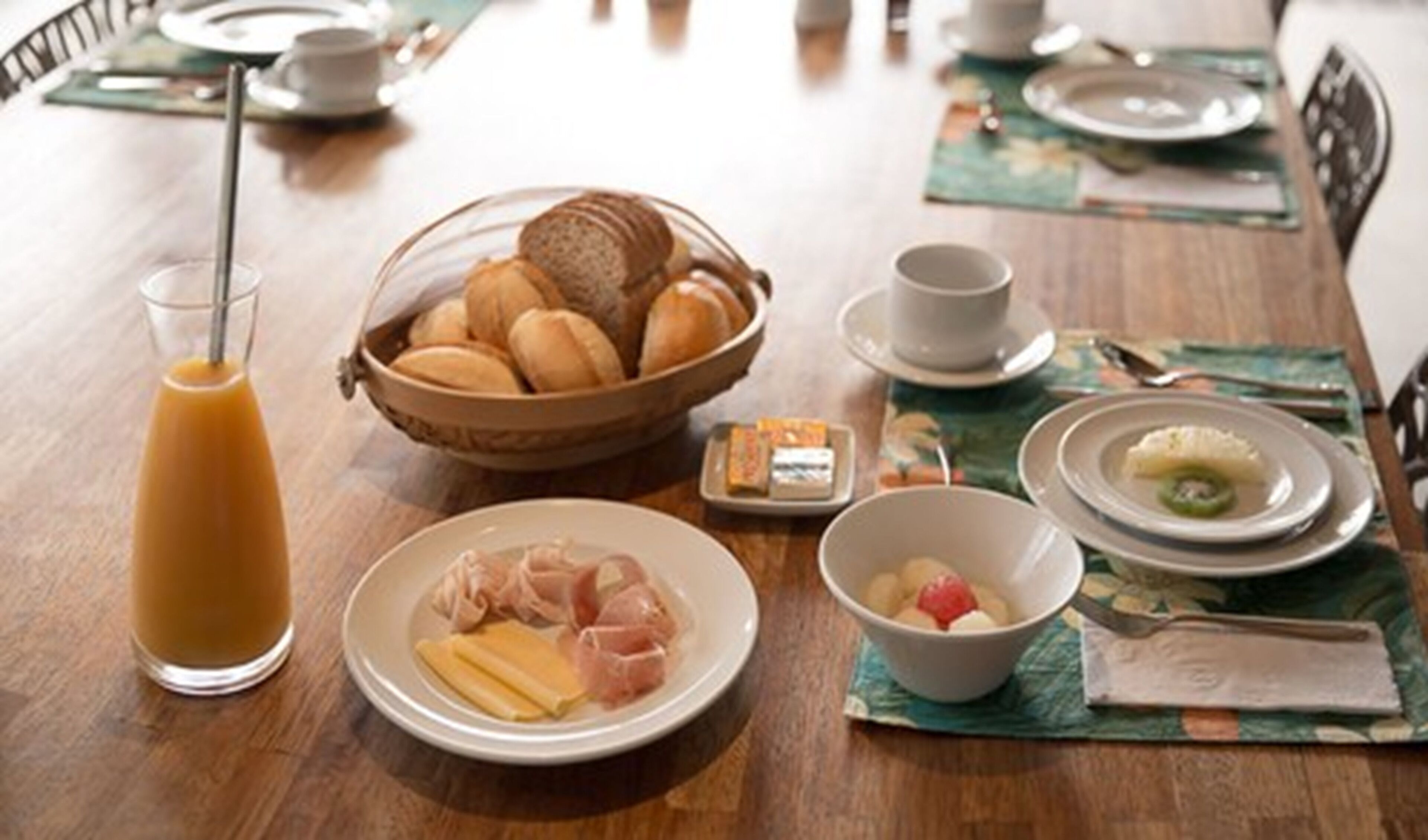 Un desayuno con pan, huevos y un bol de fruta sobre una mesa de madera.