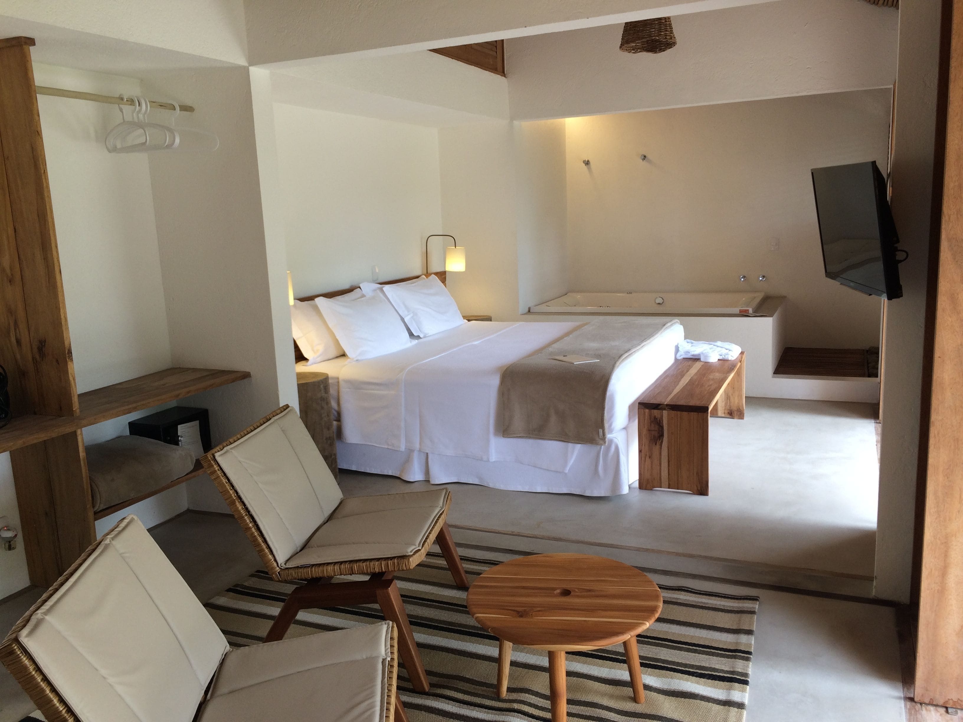 A bedroom with a bed, bedside tables, a wooden bench, a TV, and a bathroom with a bathtub and shower.